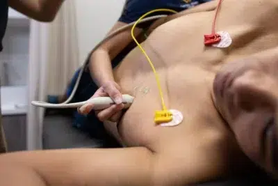 A male patient is undergoing an echocardiogram with a sonographer holding the transducer on his chest.